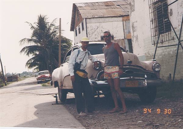 Two men beside a rusty vintage car, country road with palm tree