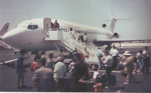 Passengers with luggage board a Tunair Boeing via airstairs on the tarmac