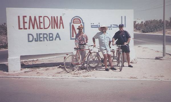 Three tourists with bicycles beside the Lemedina Djerba sign under the sun