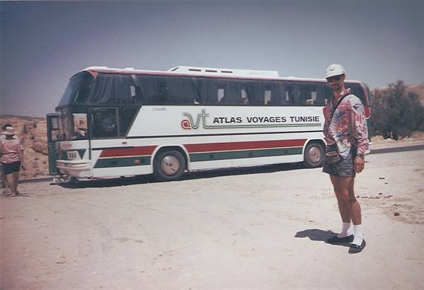 Tourist standing beside an Atlas Voyages Tunisie bus on a desert road