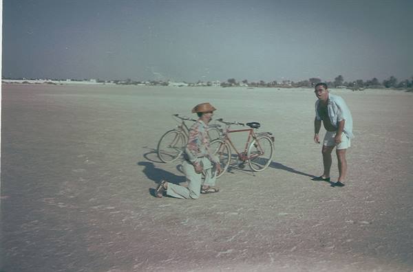 Two men with two bicycles on a sandy beach in bright sunlight