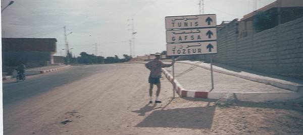 Traveler beside road signs pointing to Tozeur, Gafsa and Tunis