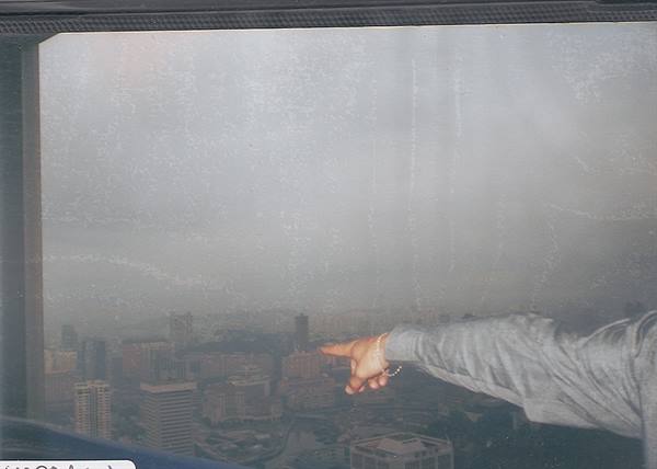 Arm in gray sweater points at hazy city from a high window