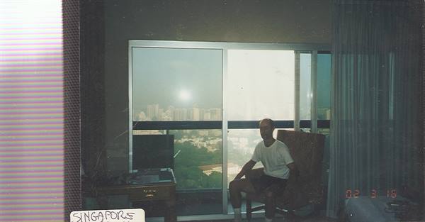 Man sitting by hotel glass door with skyscrapers behind, Singapore