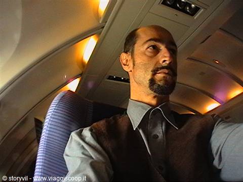 Bearded man seated inside an airplane cabin under soft cabin lights