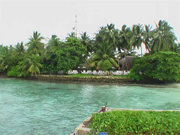 Stone jetty on turquoise lagoon, palm trees and white sun loungers on island