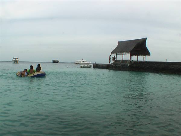 Tourists on dinghies in turquoise water near a pier with thatched hut