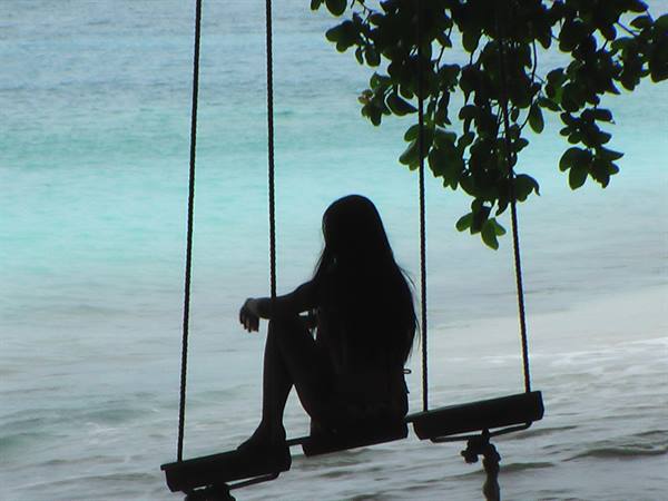 Silhouetted girl on a wooden rope swing over turquoise sea
