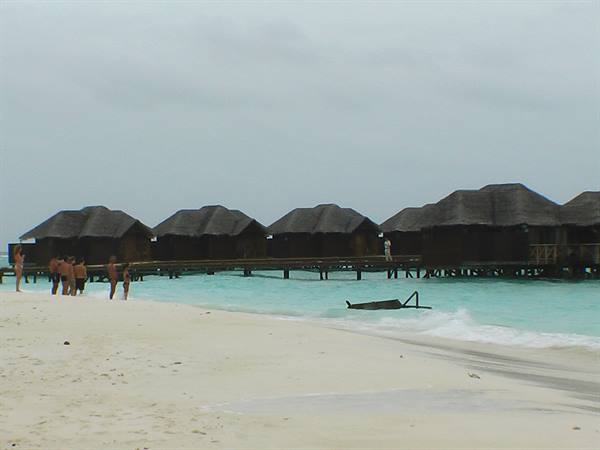 Tourists on the beach in front of stilt overwater bungalows on turquoise water