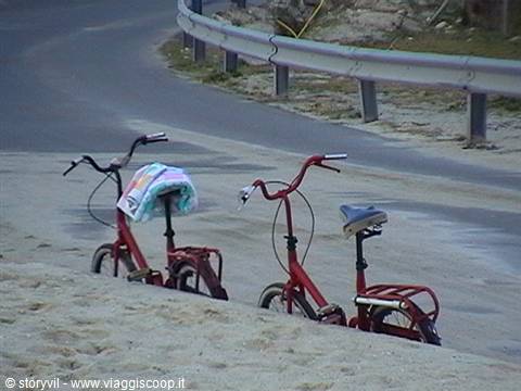 Two red bicycles parked on the sand next to the road