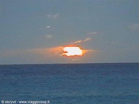 Low orange sun emerging from clouds above the open sea