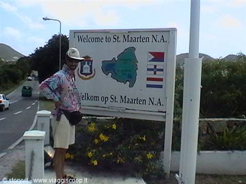 Tourist in hat next to the Welcome to St. Maarten sign with flags and map