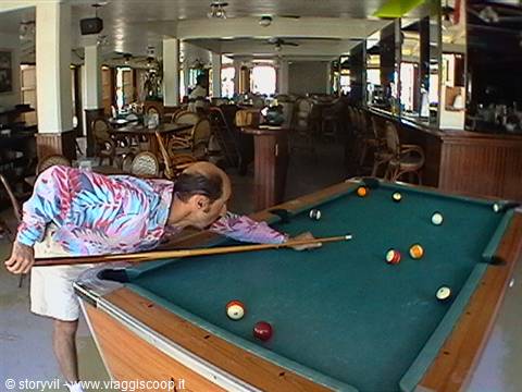 Man playing billiards in a lounge with rattan chairs and daylight