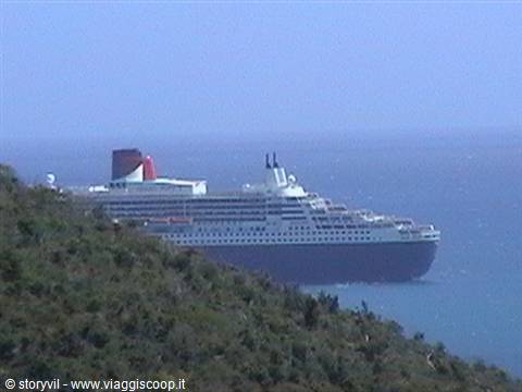 White cruise ship with red funnel sailing beside a green hill