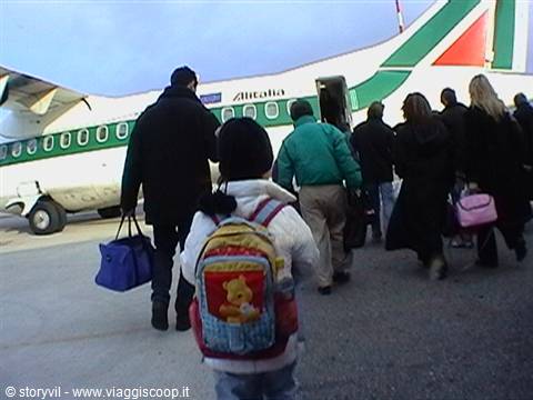 Child with backpack and passengers boarding an Alitalia plane via stairs