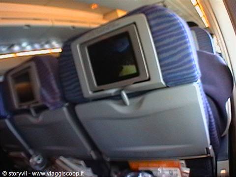 Seatback entertainment screens on blue airplane seats inside the cabin