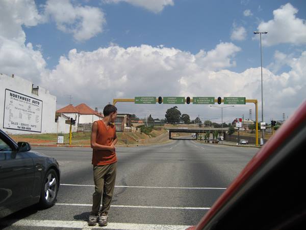 Young man in orange tank top crossing the highway between cars stopped at traffic lights