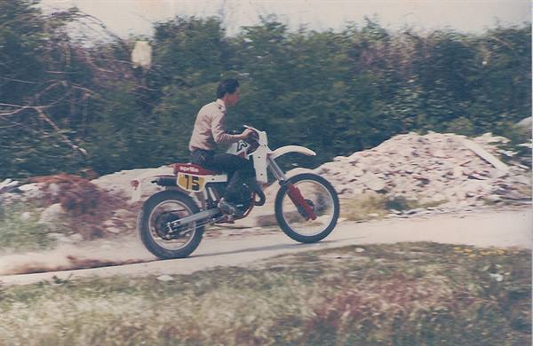 Boy riding white and red dirt bike past rubble on gravel road