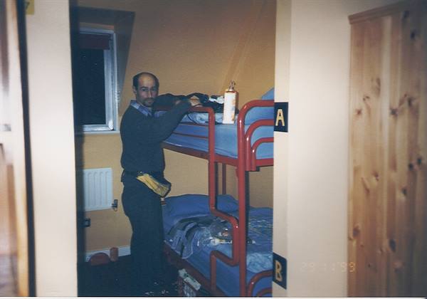Man arranging blankets on red bunk bed in hostel room