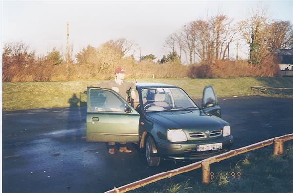 Man in cap beside a green car with open doors on wet road