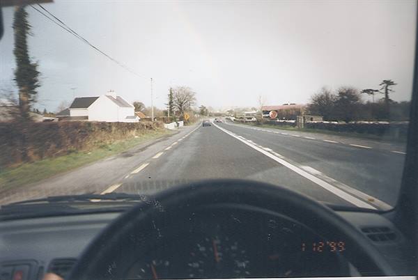 Two-lane road through the windshield, white houses and grey sky