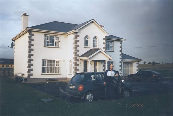 Man standing by a car in front of a two-story white house