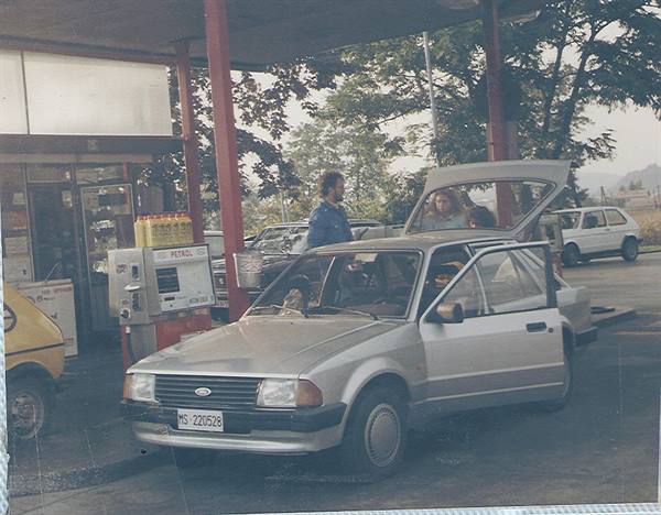 Man and woman with open hatch beside a grey Ford at a petrol station
