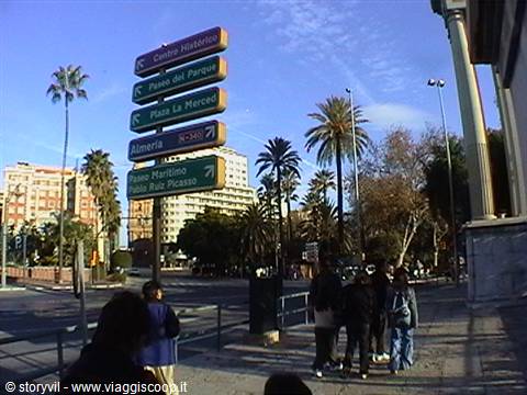 Tourists in Palma de Mallorca near road signs pointing directions among palm trees