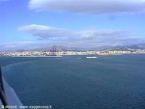 Malaga port seen from the ferry, cranes and city under clouds