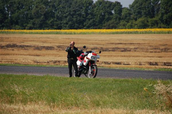 Motorcyclist with white and red bike on country road among farm fields