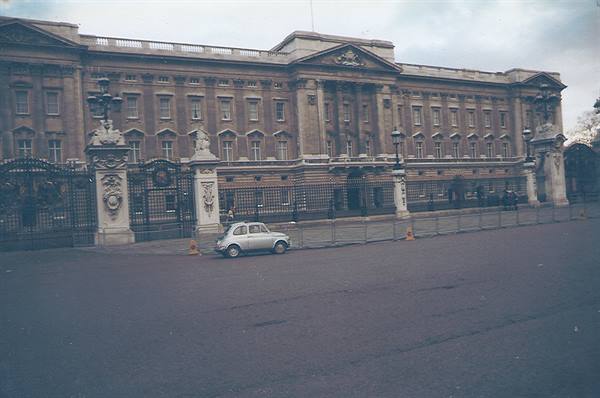 Car parked outside Buckingham Palace gates under a cloudy sky