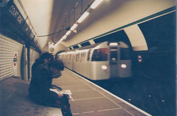 Passengers sitting on the platform at Court Road tube station as a train passes