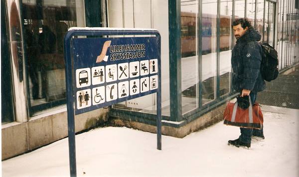 Traveler with red bag beside the Lillehammer station sign, falling snow