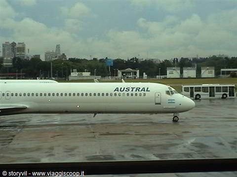 Austral ARG plane on wet tarmac with shuttle bus and skyscrapers behind