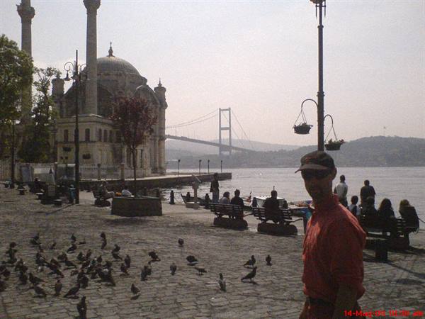 Man among pigeons in front of Ortaköy Mosque and the Bosphorus Bridge