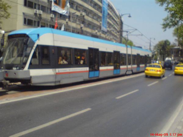 White and blue tram running along the avenue, yellow taxis beside