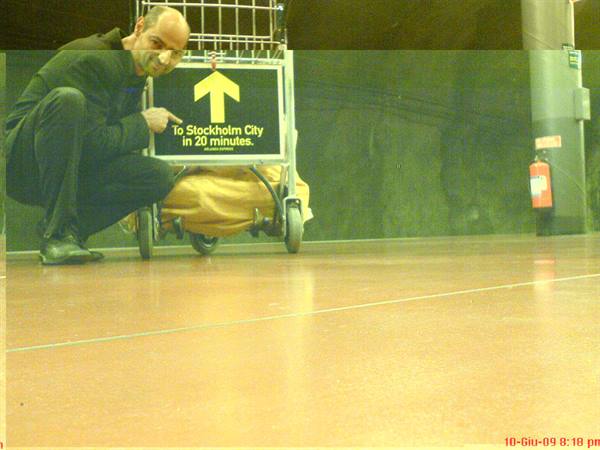 Man crouching points at luggage trolley sign, direction Stockholm