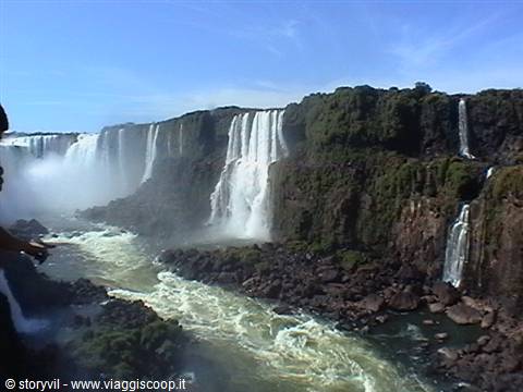 Iguazú Falls, water cascades over dark rocks amid green vegetation, mist rising below