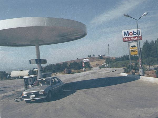 Gray car refueling at Mobil station with round canopy along rural road