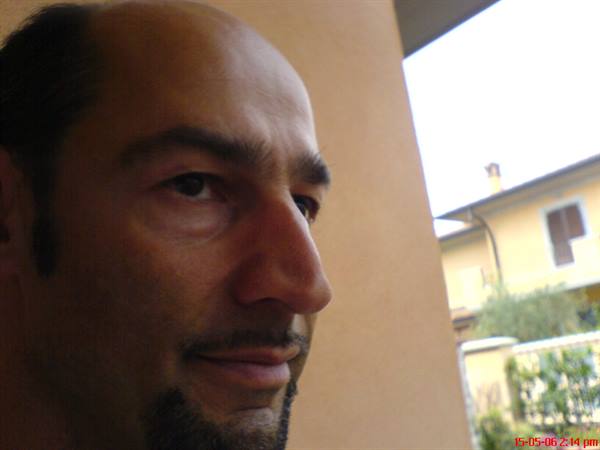 Close-up of a smiling man with goatee, yellow house in the background