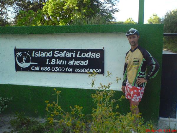 Cyclist beside the black Island Safari Lodge sign, painted green wall