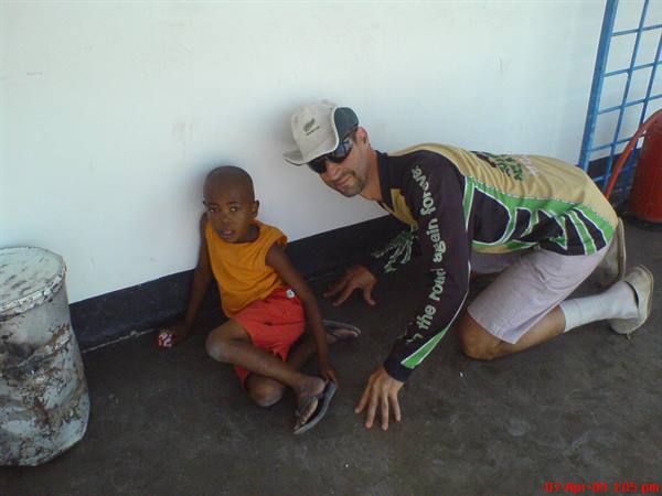 Cyclist tourist kneels beside a young boy sitting on concrete floor