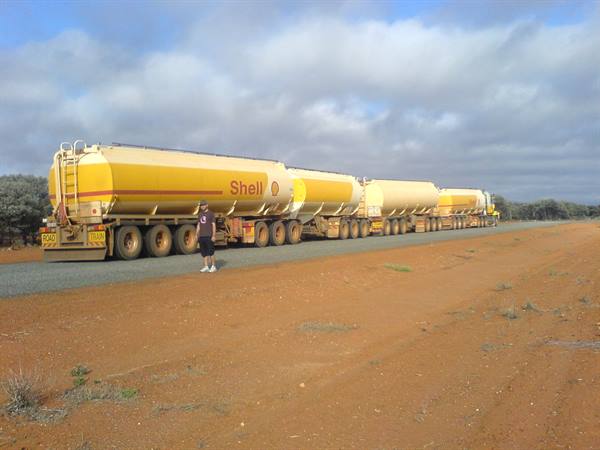 Shell road train with four yellow tankers on red dirt track, man nearby