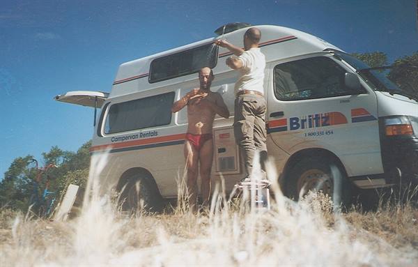 Two men beside a Britz campervan, one in red underwear, dry grass, blue sky