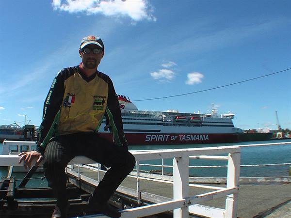 Cyclist posing on metal footbridge, Spirit of Tasmania ferry docked behind