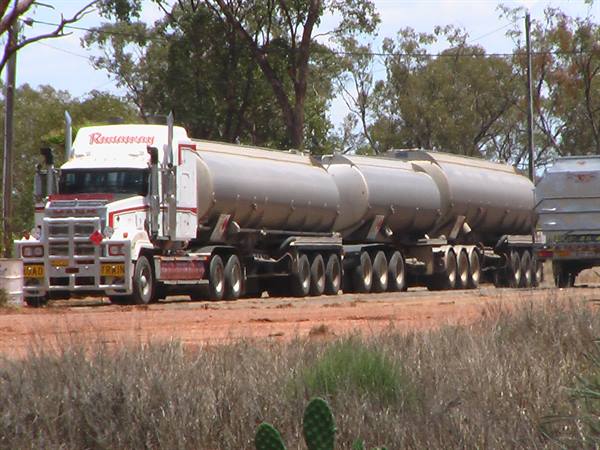 White road train tanker truck on red dirt road, dry bush and trees