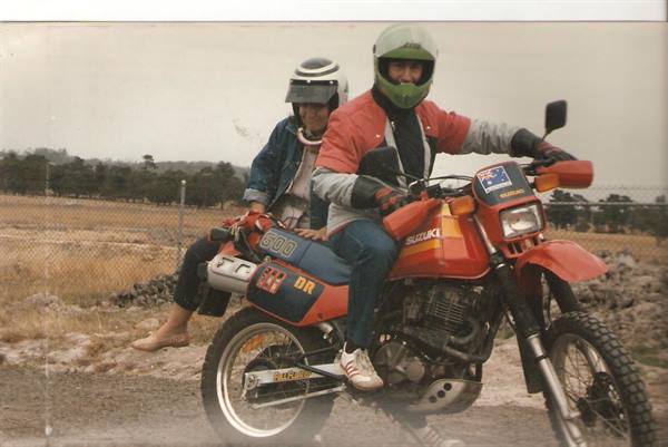 Two helmeted riders on a red Suzuki DR 600 on a dirt road