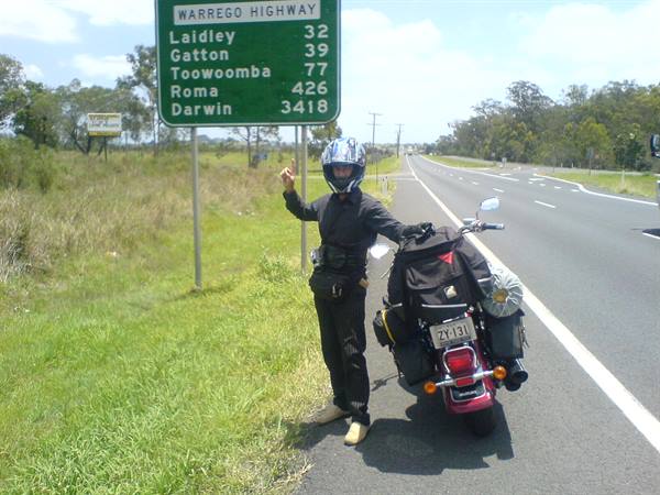 Helmeted rider beside loaded motorcycle under the Warrego Highway sign