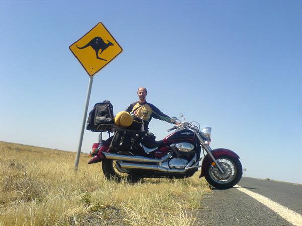 Motorcyclist beside kangaroo road sign on a desert highway