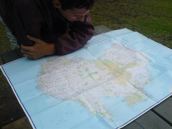 Man studies a paper map spread on a wooden table outdoors